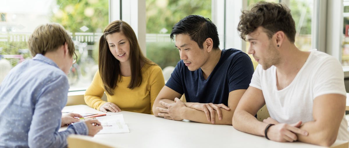 4 Studierende sitzen arbeitend an einem Tisch